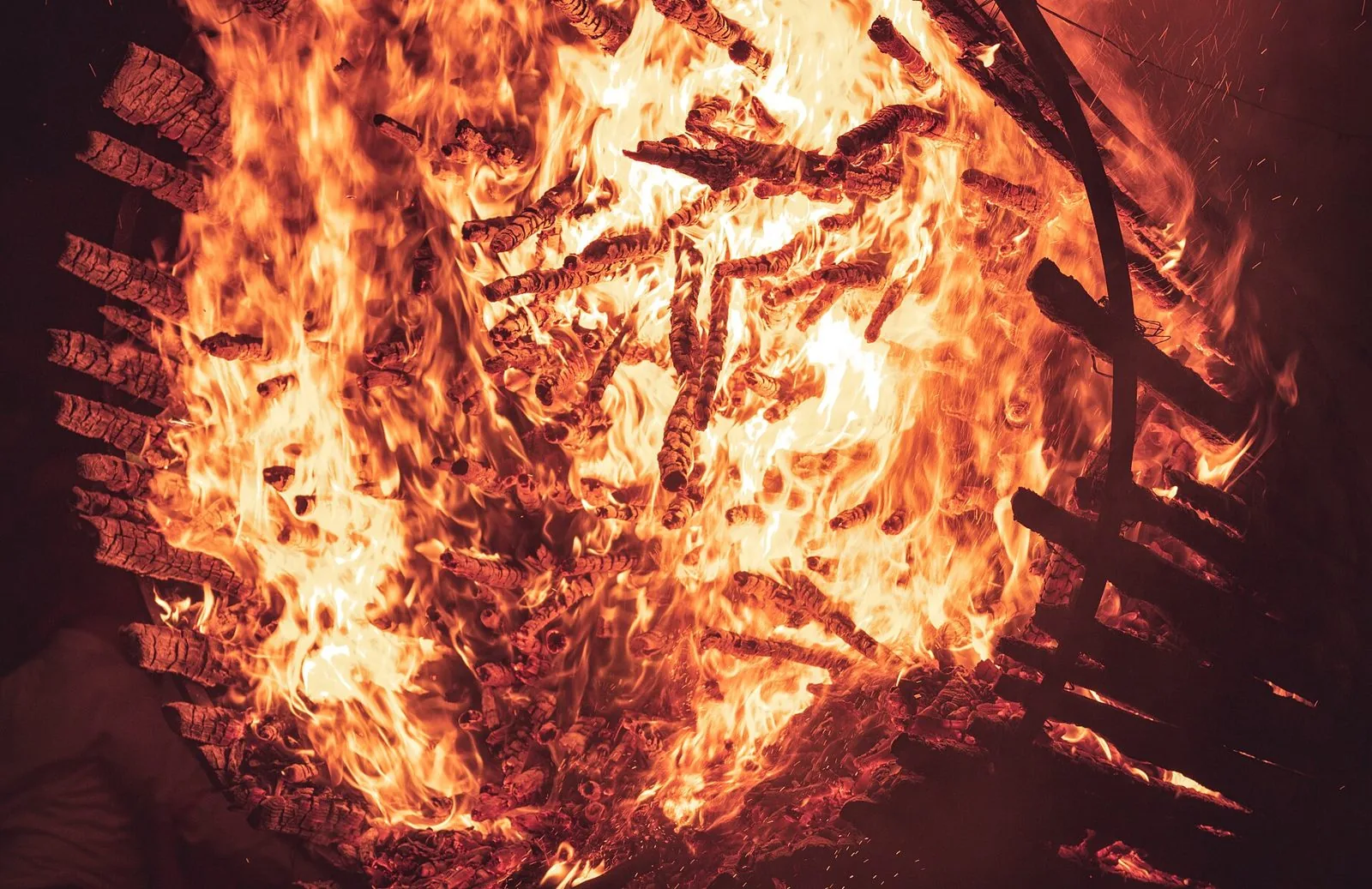 Primo piano di una fracchia in fiamme: la struttura conica di assi di legno avvolta dal fuoco e dalle braci