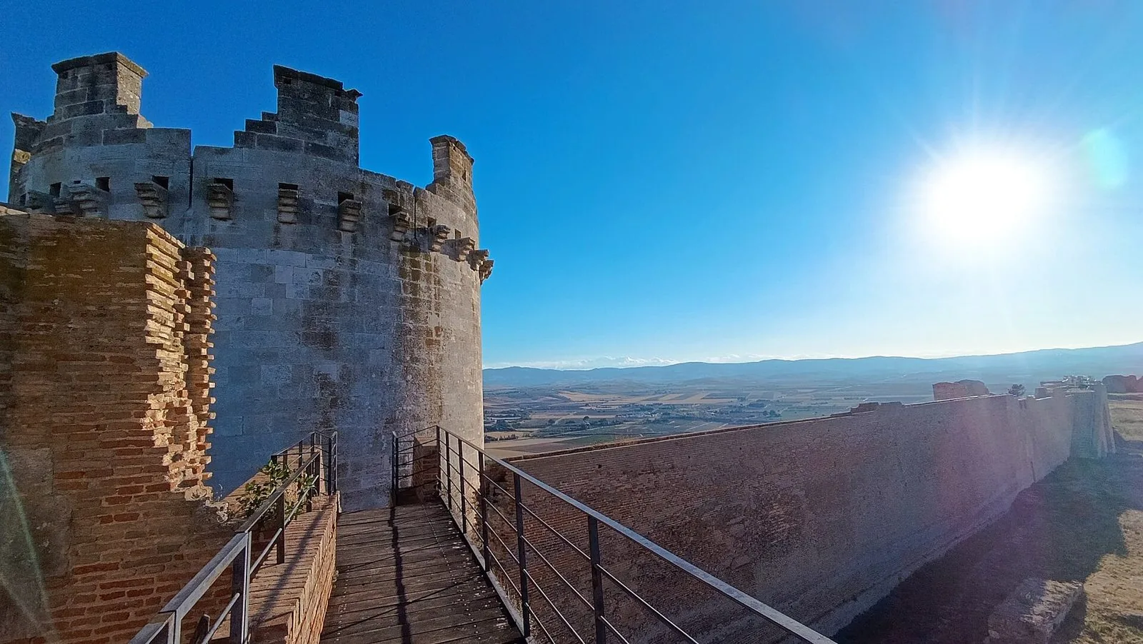 Una torre e le mura della Fortezza svevo-angioina di Lucera, con la passerella in legno e la vista sulla pianura e sulle colline all'orizzonte